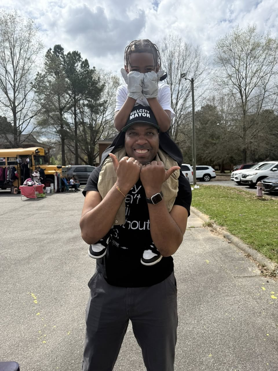 Durham Mayor Leonardo Williams is shown with a child on his head, both displaying Bull City hands.