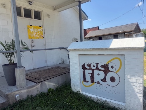 A white building and white sign outside of it, which reads Coco Fro