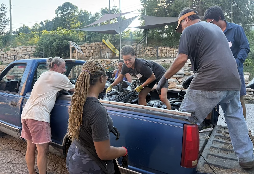 Volunteers in the back of a pickup truck, unloading garbage bags