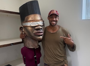Pierce Freelon poses with a life-size mascot, Orion, who is wearing futuristic glasses