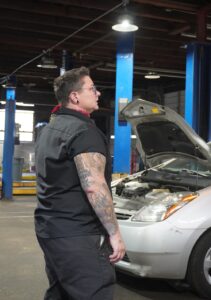 A person in an auto shop with a hood open on a silver car