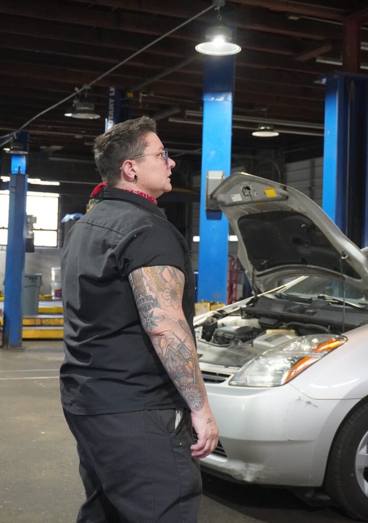 A person in an auto shop with a hood open on a silver car