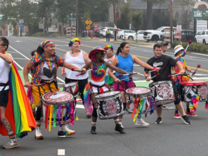 Drummers, adorned in bright clothing, march through a street.