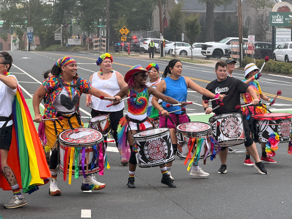Drummers, adorned in bright clothing, march through a street.